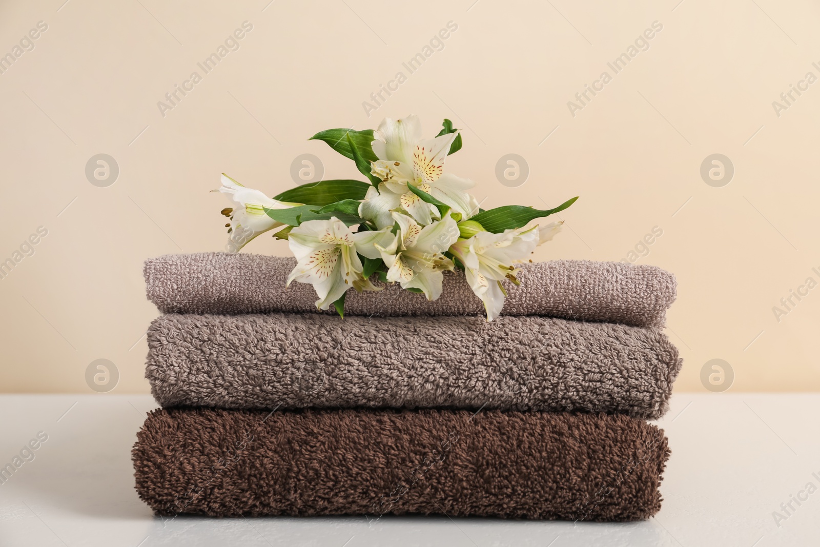 Stack of soft towels and lilies on white table against beige background, closeup Photo of Stack of soft towels and lilies on white table against beige background, closeup