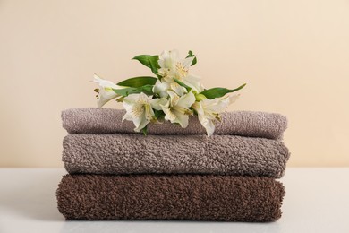 Photo of Stack of soft towels and lilies on white table against beige background, closeup