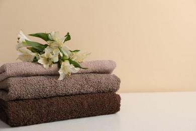 Photo of Stack of soft towels and lilies on white table against beige background, closeup. Space for text