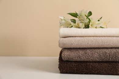 Photo of Stack of soft towels and lilies on white table against beige background, closeup. Space for text