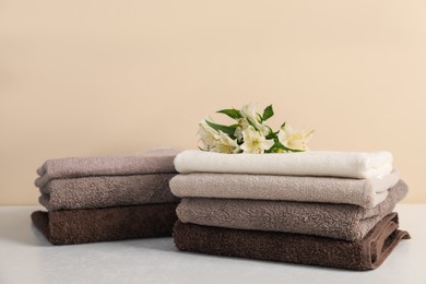 Photo of Stack of soft towels and lilies on white table against beige background