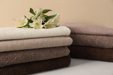 Photo of Stack of soft towels and lilies on white table against beige background, closeup