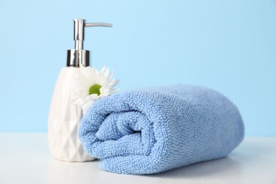 Photo of Soft towel, liquid soap and chrysanthemum flower on table against light blue background, closeup