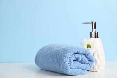 Photo of Soft towel, liquid soap and chrysanthemum flower on table against light blue background, space for text