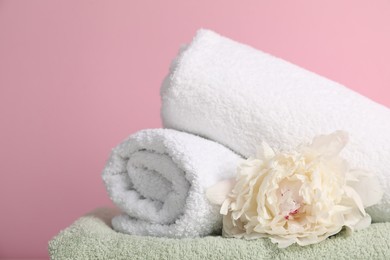 Photo of Stack of soft towels and peony flower on pink background, closeup