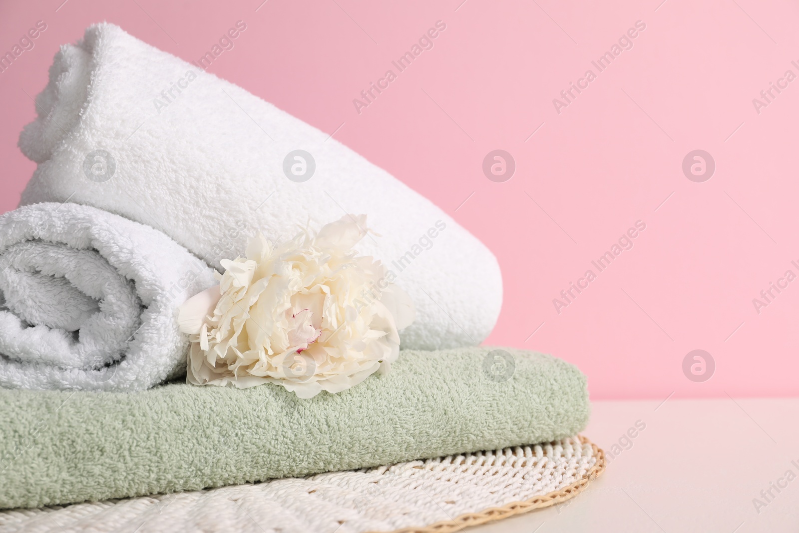 Stack of soft towels and peony flower on table against pink background, closeup. Space for text Photo of Stack of soft towels and peony flower on table against pink background, closeup. Space for text