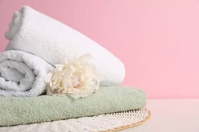 Photo of Stack of soft towels and peony flower on table against pink background, closeup. Space for text