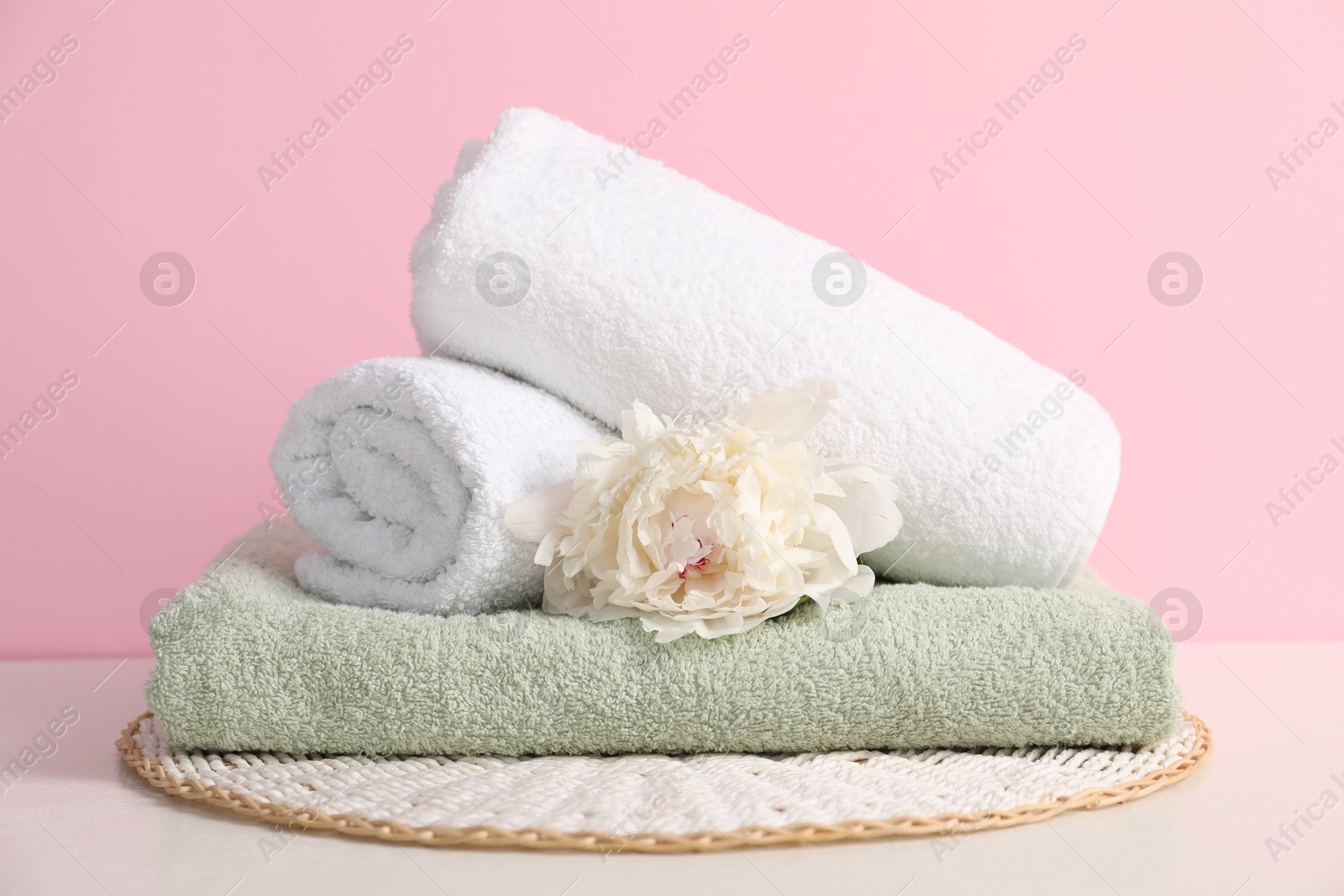 Stack of soft towels and peony flower on table against pink background Photo of Stack of soft towels and peony flower on table against pink background