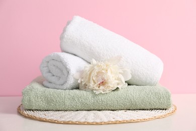 Photo of Stack of soft towels and peony flower on table against pink background