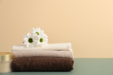Photo of Stack of soft towels, cosmetic product and chrysanthemum flowers on color background, closeup. Space for text