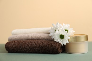 Photo of Stack of soft towels, cosmetic product and chrysanthemum flowers on color background, closeup