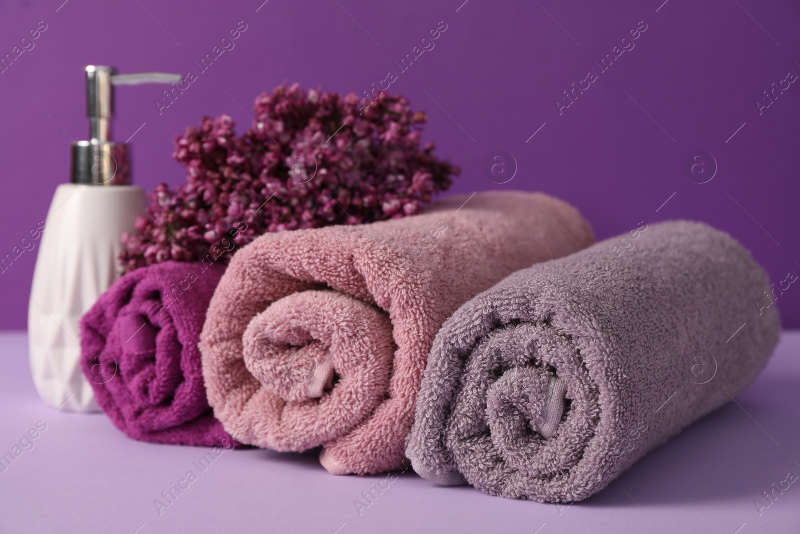 Soft towels, liquid soap and lilac flowers on violet background, closeup Photo of Soft towels, liquid soap and lilac flowers on violet background, closeup
