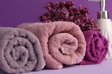 Photo of Soft towels, liquid soap and lilac flowers on violet background, closeup