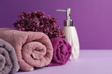 Photo of Soft towels, liquid soap and lilac flowers on violet background, closeup. Space for text