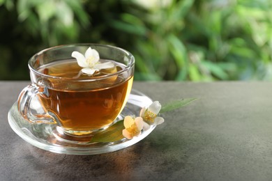 Photo of Aromatic jasmine tea in glass cup and flowers on grey table outdoors, closeup. Space for text