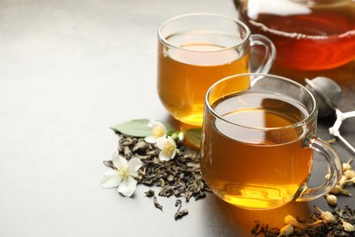 Photo of Aromatic jasmine tea in glass cups, brew and flowers on grey table, closeup. Space for text