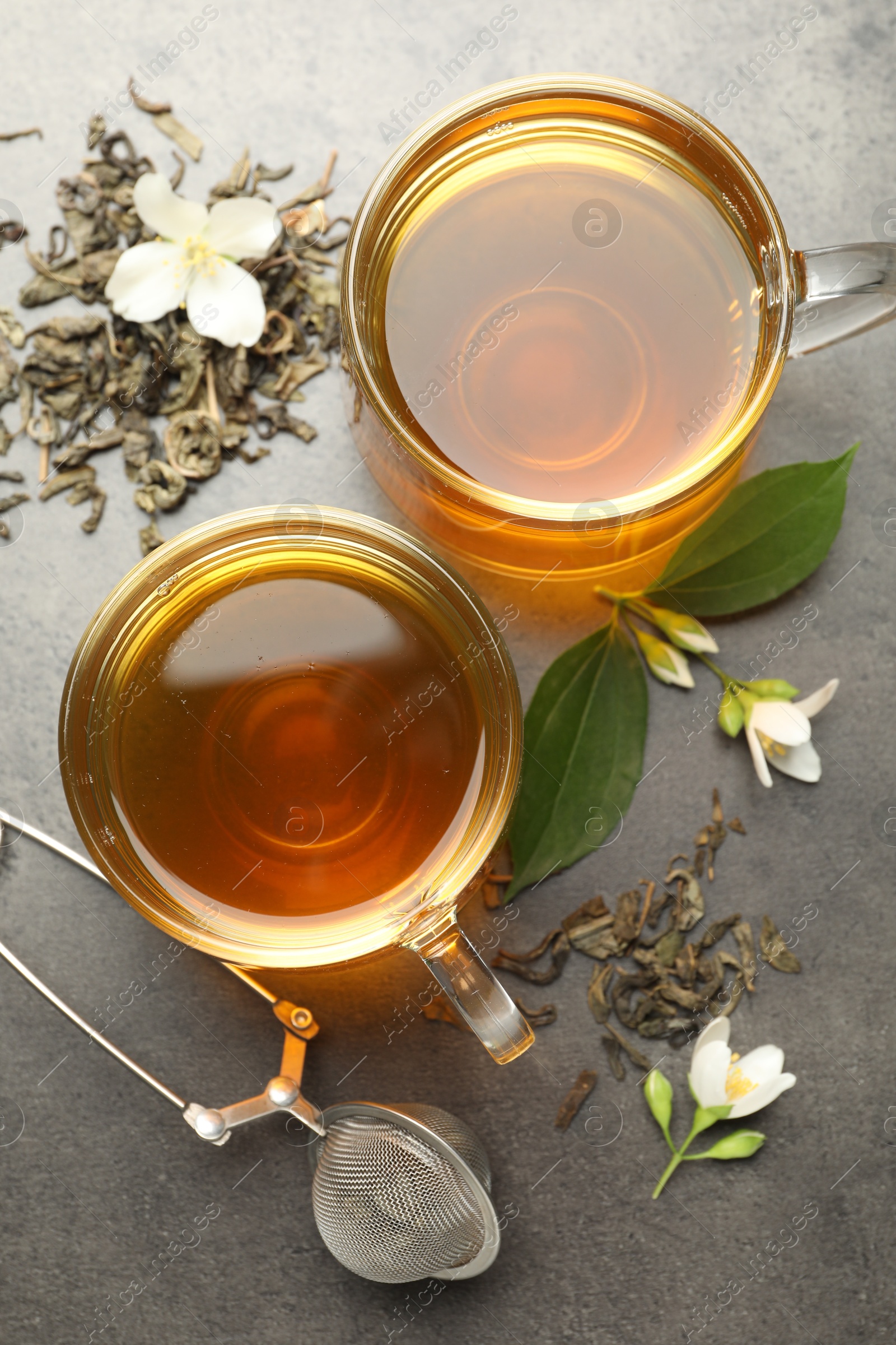 Aromatic jasmine tea in glass cups, brew and flowers on grey table, flat lay Photo of Aromatic jasmine tea in glass cups, brew and flowers on grey table, flat lay