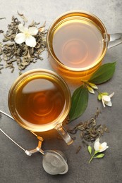 Photo of Aromatic jasmine tea in glass cups, brew and flowers on grey table, flat lay