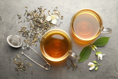 Photo of Aromatic jasmine tea in glass cups, brew and flowers on grey table, flat lay