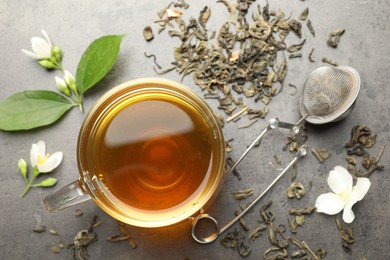 Photo of Aromatic jasmine tea in glass cup, brew and flowers on grey table, flat lay
