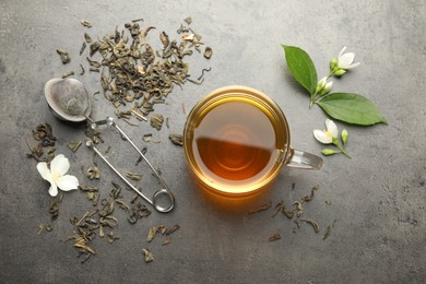 Photo of Aromatic jasmine tea in glass cup, brew and flowers on grey table, flat lay