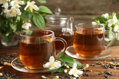 Photo of Aromatic jasmine tea in glass cups, teapot, brew and flowers on wooden table, closeup