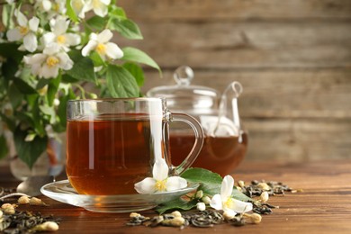 Photo of Aromatic jasmine tea in glass cups, teapot, brew and flowers on wooden table, closeup. Space for text
