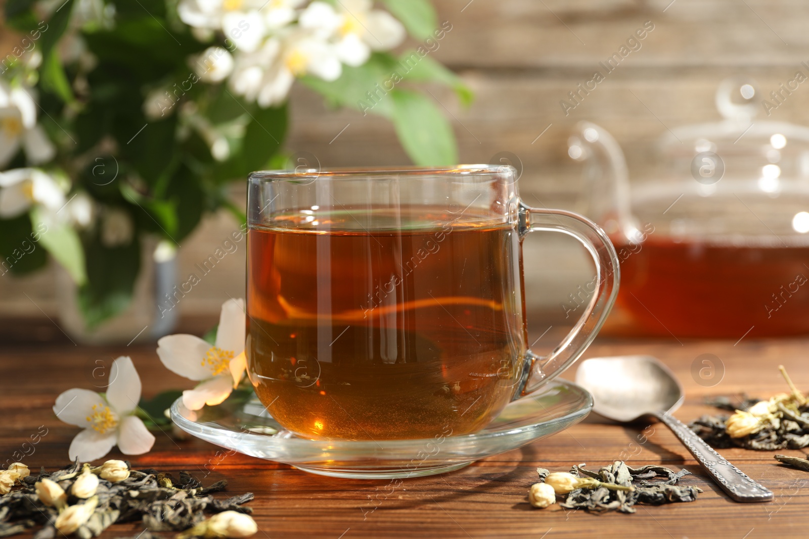 Aromatic jasmine tea in glass cup, brew and flowers on wooden table, closeup Photo of Aromatic jasmine tea in glass cup, brew and flowers on wooden table, closeup