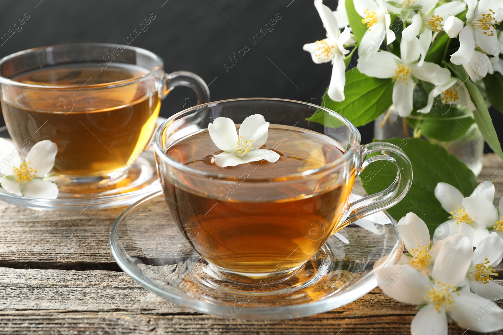 Photo of Aromatic jasmine tea in glass cups, flowers and green leaves on wooden table, closeup
