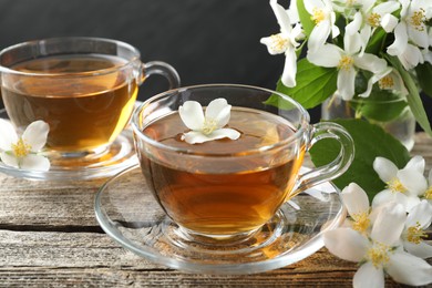 Photo of Aromatic jasmine tea in glass cups, flowers and green leaves on wooden table, closeup