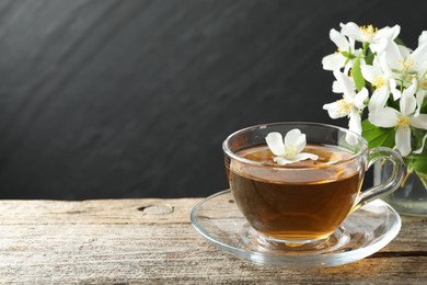 Photo of Aromatic jasmine tea in glass cup, flowers and green leaves on wooden table, closeup. Space for text