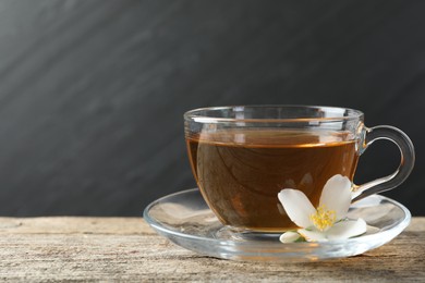 Photo of Aromatic jasmine tea in glass cup and flower on wooden table, closeup. Space for text
