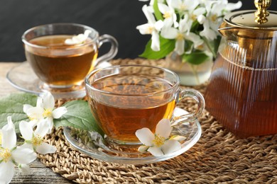 Photo of Aromatic jasmine tea in glass cups, flowers and teapot on table, closeup