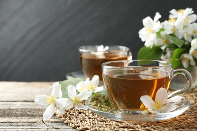 Photo of Aromatic jasmine tea in glass cups, flowers and green leaves on wooden table, closeup. Space for text