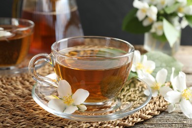 Photo of Aromatic jasmine tea in glass cup and flowers on wooden table, closeup