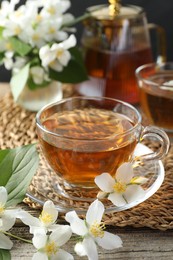 Photo of Aromatic jasmine tea and flowers on wooden table, closeup