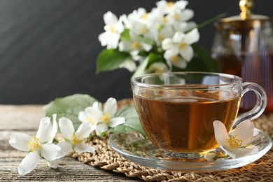 Photo of Aromatic jasmine tea and flowers on wooden table, closeup