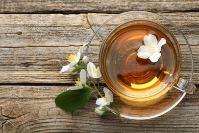 Photo of Aromatic jasmine tea in glass cup, flowers and green leaf on wooden table, flat lay. Space for text