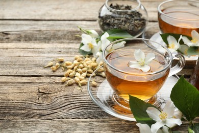 Photo of Aromatic jasmine tea in glass cups, brew and flowers on wooden table, closeup. Space for text