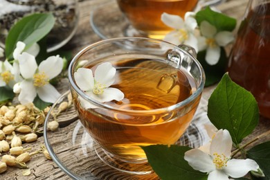 Photo of Aromatic jasmine tea in glass cups, brew and flowers on wooden table, closeup