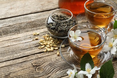 Photo of Aromatic jasmine tea in glass cups, brew and flowers on wooden table, closeup. Space for text