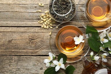 Photo of Aromatic jasmine tea in glass cups, teapot, brew and flowers on wooden table, flat lay. Space for text
