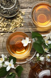 Photo of Aromatic jasmine tea in glass cups, teapot, brew and flowers on wooden table, flat lay