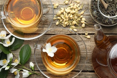 Photo of Aromatic jasmine tea in glass cups, teapot, brew and flowers on wooden table, flat lay