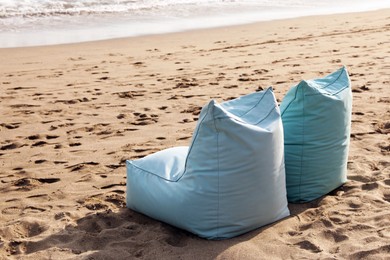 Photo of Light blue bean bag chairs on sandy beach by sea