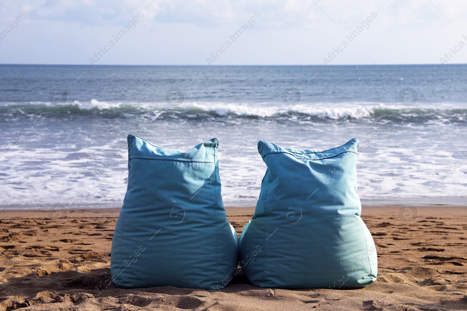 Light blue bean bag chairs on sandy beach by sea Photo of Light blue bean bag chairs on sandy beach by sea