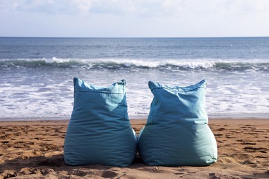 Photo of Light blue bean bag chairs on sandy beach by sea