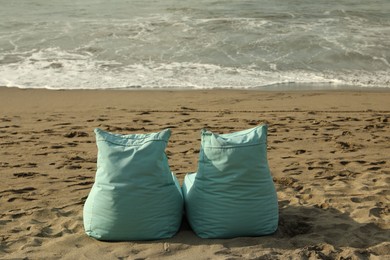Photo of Turquoise bean bag chairs on sandy beach by sea
