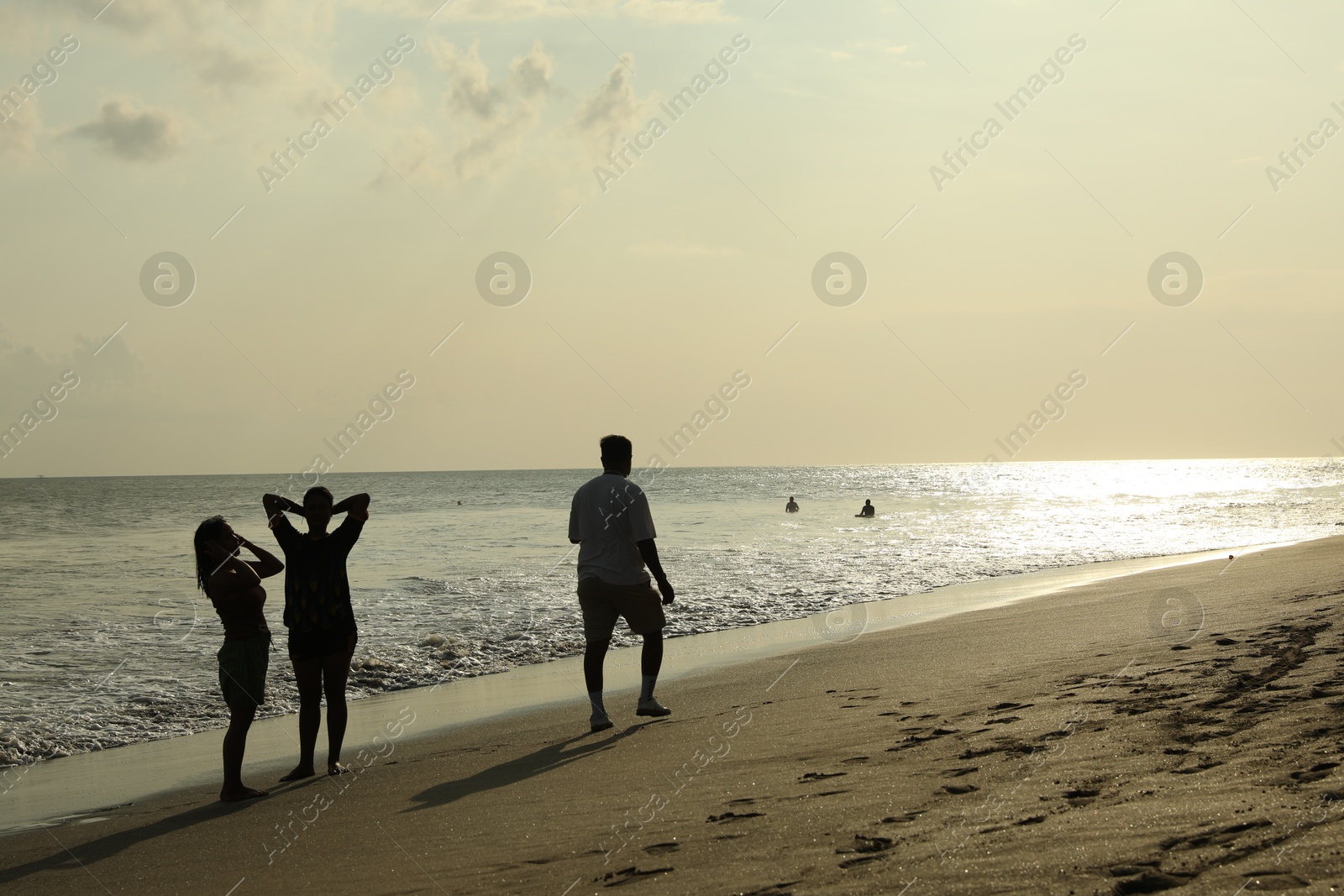 Bali, Indonesia - May 20, 2025: Man walking along seashore and women enjoying sunset by sea Photo of Bali, Indonesia - May 20, 2025: Man walking along seashore and women enjoying sunset by sea