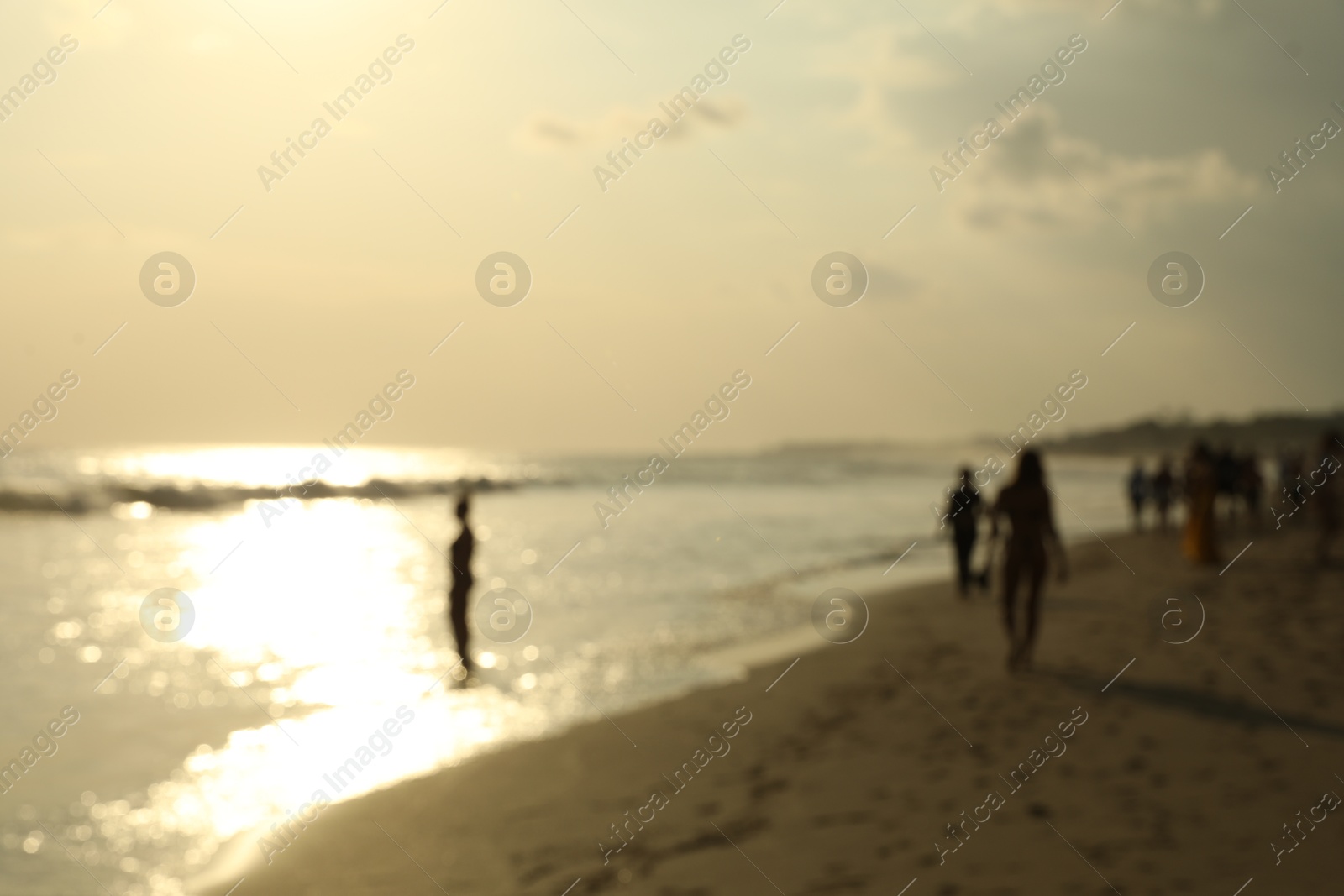 Blurred view of sandy beach with people walking near sea Photo of Blurred view of sandy beach with people walking near sea